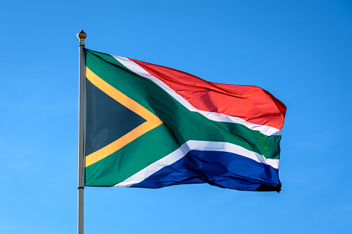 The flag of South Africa is flying in the wind at full mast against blue sky.
